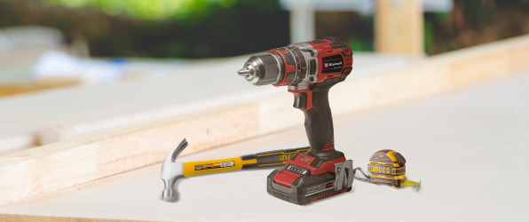 Kit de herramientas básicas de construcción con taladro, martillo y cinta métrica sobre una superficie de madera.