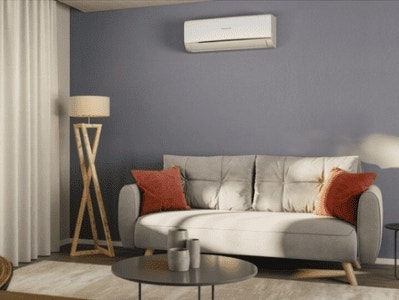 Sala de estar acogedora con aire acondicionado, sofá gris y cojines decorativos en tonos cálidos.