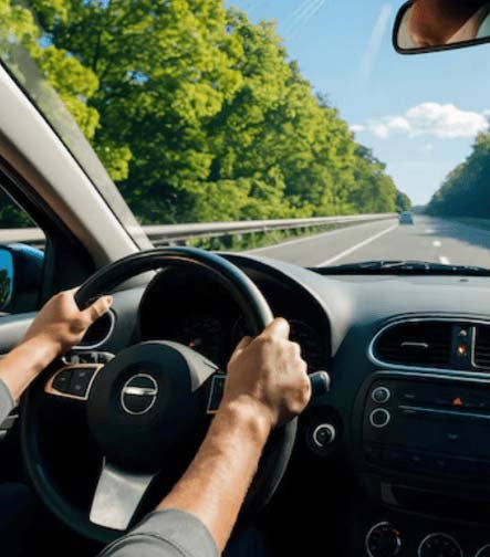 Conductor manejando un automóvil en carretera rodeada de naturaleza