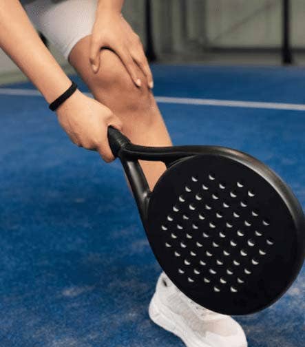 Jugador de pádel en una cancha azul sosteniendo su rodilla y una pala negra.