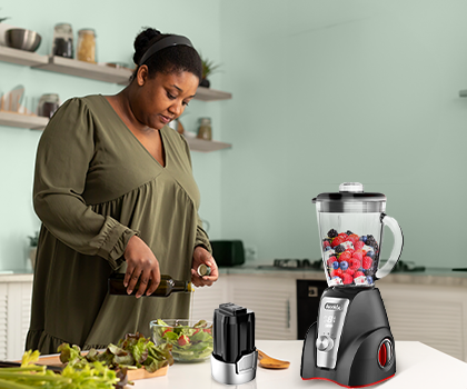 Mujer preparando alimentos con licuadora y procesador en una cocina moderna.