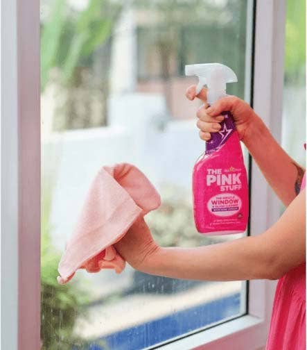 Persona limpiando una ventana con spray The Pink Stuff y paño de microfibra