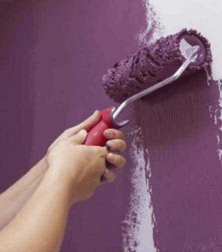 Persona pintando una pared con rodillo y pintura morada.